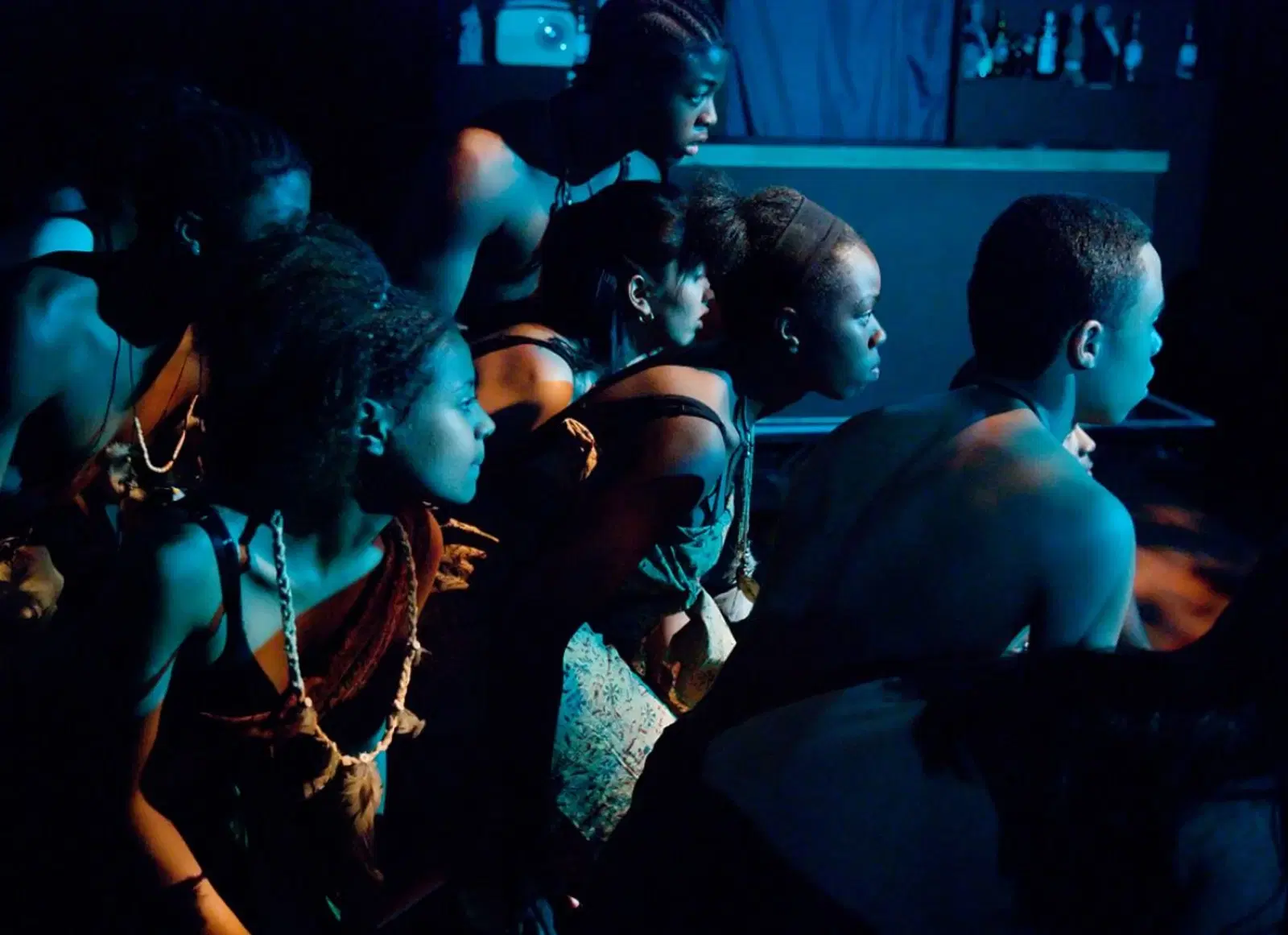 A group of performers in traditional african attire engrossed in a moment backstage, lit by the ambient stage lighting.