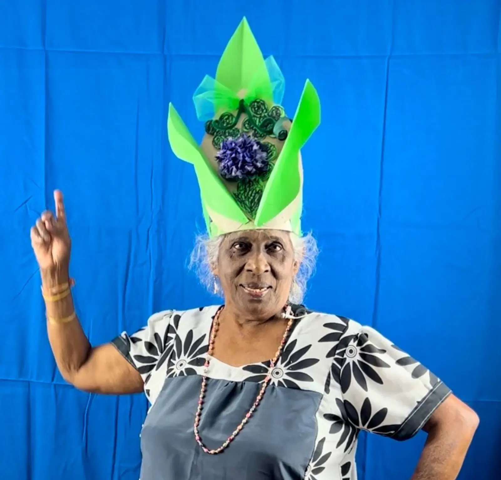 A person wearing a costume headdress with a floral and feather design poses confidently against a blue background.