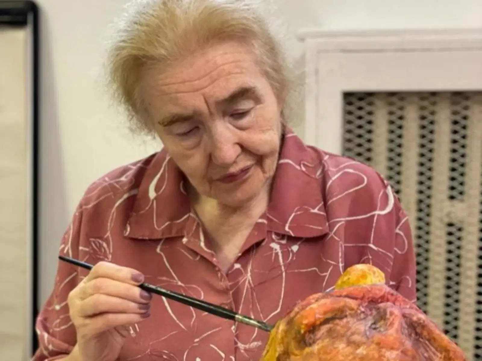 An elderly woman concentrates on painting, carefully applying brushstrokes to her artwork.