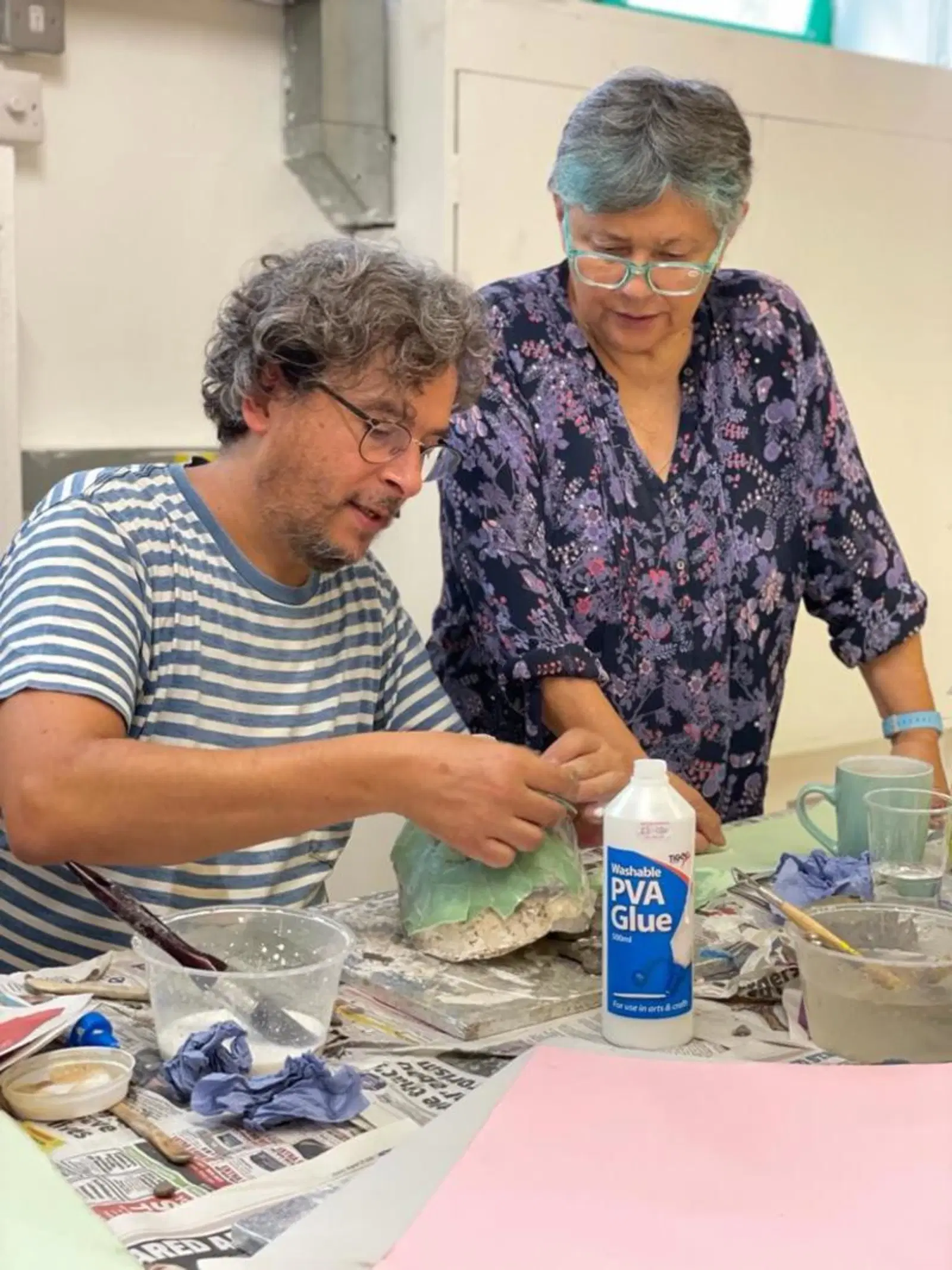 Creativity in action: a man and woman deeply focused while collaboratively working on a craft project involving paper mache and glue in an art workshop.